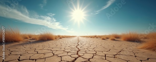 Cracked dry earth stretches to horizon under bright sun. Sparse golden grass grows in arid wasteland. Vast empty landscape symbolizes drought, extreme weather, and climate crisis.