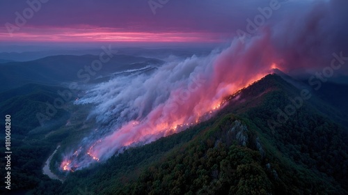 Aerial view of a mountain range ablaze at sunset, smoke billowing across the landscape