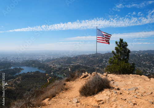 Flag of the United States of America waving on Cahuenga Peak at Wisdom Tree with the Hollywood Reservoir and skyline of LA in the background during a summer season in Los Angeles, California, USA