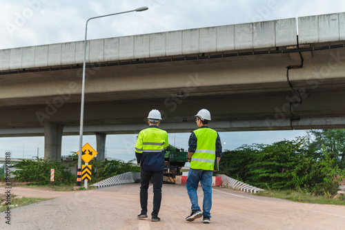 Construction Workers Inspecting Bridge Infrastructure on a Roadway Under an Elevated Highway in Daylight with Safety Gear and Traffic Signs