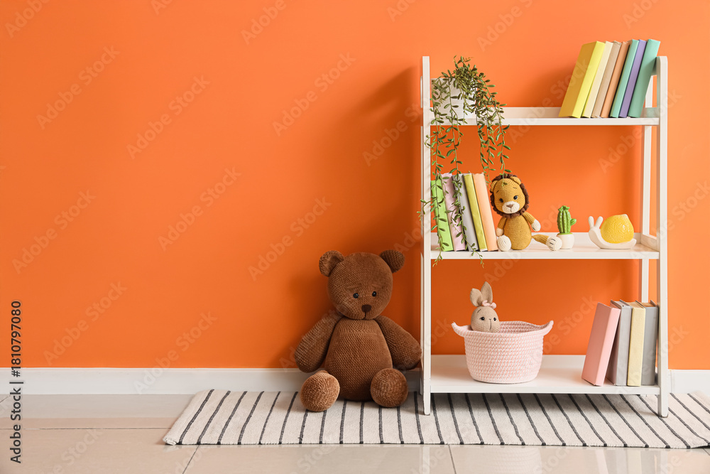 Naklejka premium Bookshelf with toys and plant near orange wall in children's room
