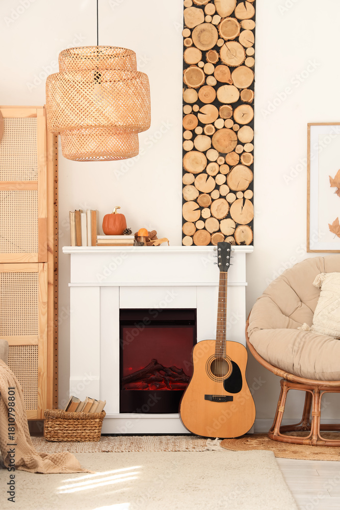 Fototapeta premium Interior of living room with armchair, closet, guitar, fireplace and autumn home decor near white wall