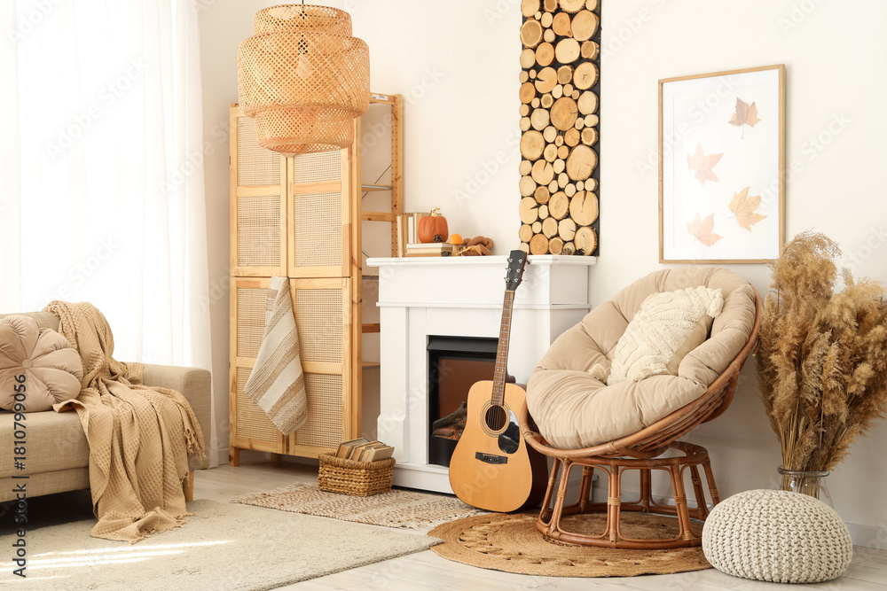 Fototapeta premium Interior of living room with sofa, armchair, closet, guitar, fireplace and autumn home decor near white wall