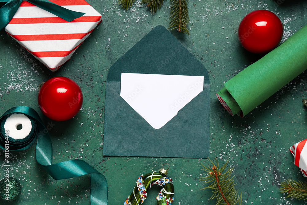 Naklejka premium Blank greeting card in envelope with Christmas decorations, gift box and packing materials on grunge green background