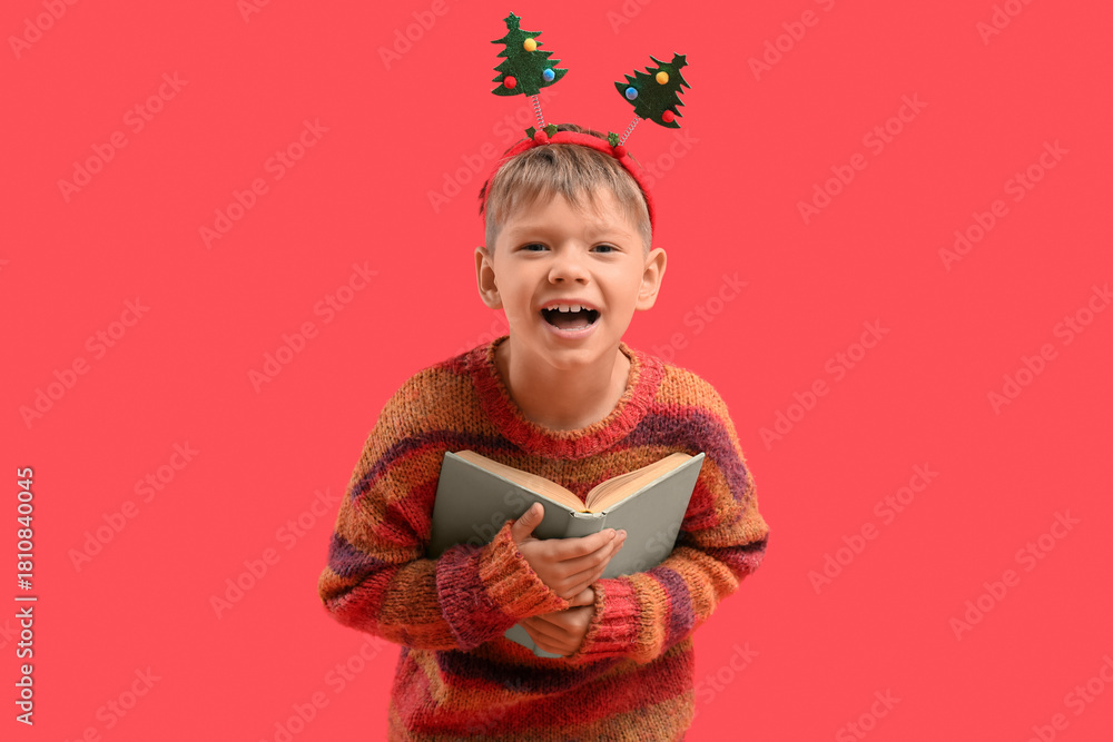Naklejka premium Cute little boy with book on red background. Christmas celebration