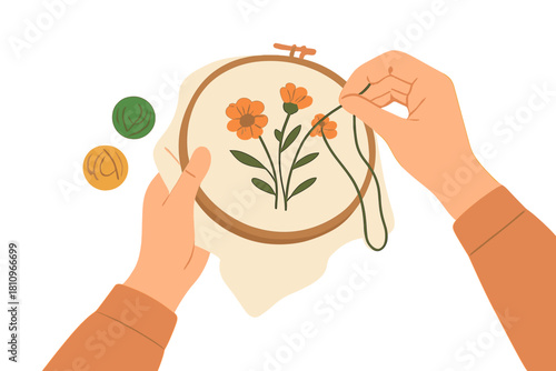 Hands embroidering orange flowers in wooden hoop with thread spools