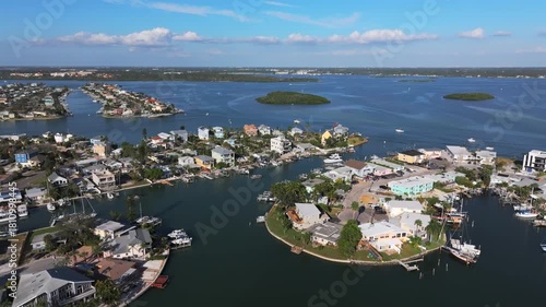 Aerial drone establishing shot of luxury waterfront neighborhood along Boca Ciega Bay near Jack's Boat Basin, featuring colorful homes with private docks on a canal in Saint Pete Beach, Florida.