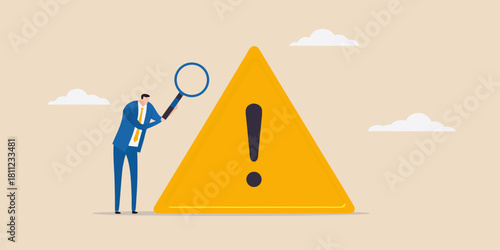 Business man inspecting warning sign with magnifying glass for risk management