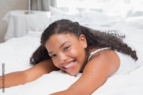 African American child girl lying on white duvet smiling at camera, wearing white sleeveless top