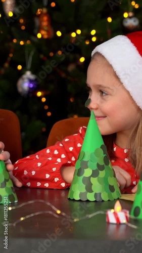 Happy children fun make diy from paper Christmas tree and stick stickers on nose. Holidays craft. New Years festive decorations. Vertical shot
