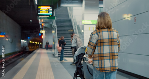 Mother waiting patiently with baby stroller on subway platform, capturing urban commute and family lifestyle through natural light