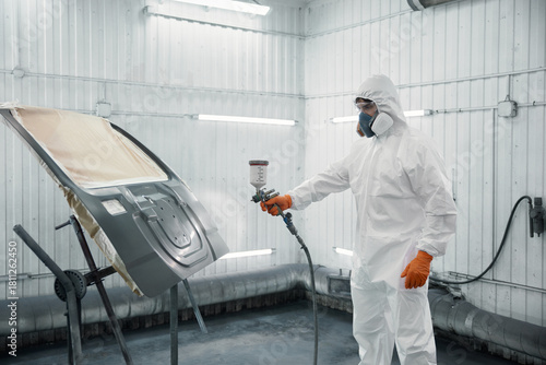An automotive technician is spray-painting a car panel in a protective paint booth