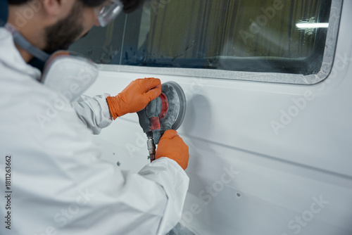 Auto body technician sanding van with orbital sander for paint preparation and repair