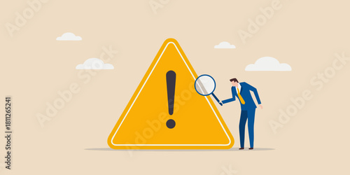 Businessman using magnifying glass to inspect a yellow warning sign