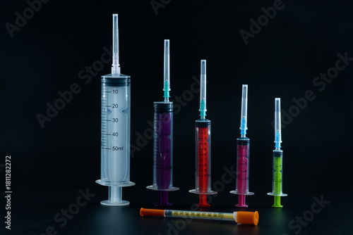 A composition of various size syringes on a dark background, highlighting themes of measurement, vaccination, and lab work.