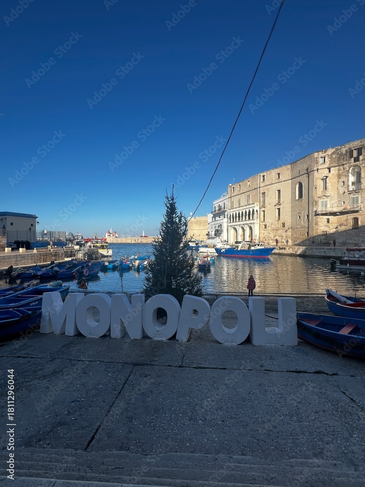 Fototapeta premium Monopoli harbor view: Capturing the unique harbor view with the city name as the focal point, embracing the atmosphere of a beautiful day under the blue sky. 