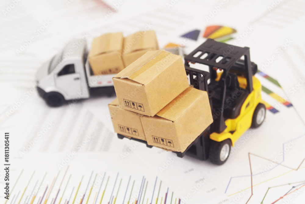 Obraz premium Lorry truck with cardboard boxes and forklift on reports with financial figures. Management of shipping, delivery, cargo, moving and freight transportation concept