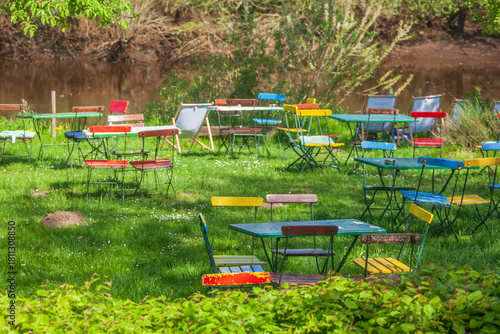 Fototapeta Naklejka Na Ścianę i Meble -  Bunte Stühle und Tische eines Cafes auf einer Rasenfläche an einem Fluss, Gastronomie, Deutschland, Europa