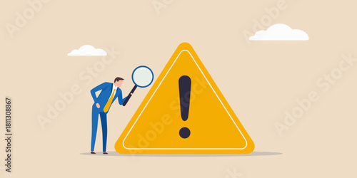 Businessman with magnifying glass inspecting a large exclamation point warning sign