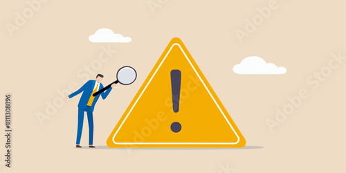 Businessman with magnifying glass inspects large yellow warning sign