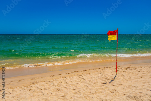 Red and yellow flag on sandy beach of Tavira Algarve Portugal