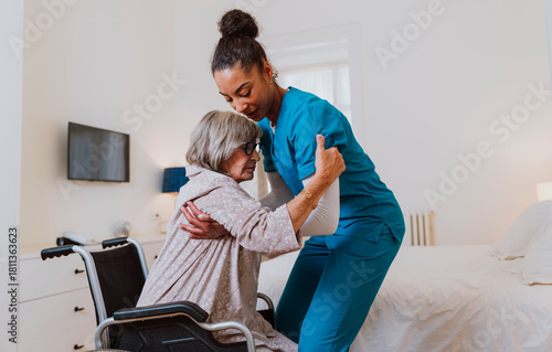 Caregiver assisting senior with transfer from wheelchair to bed at home