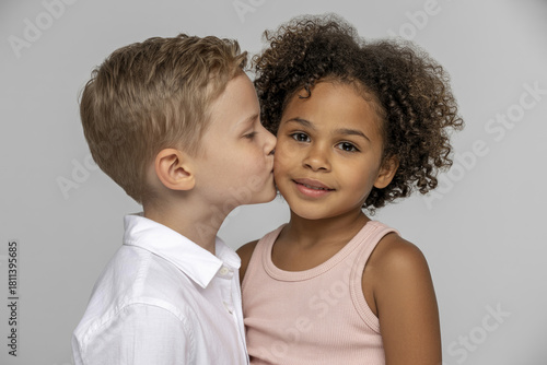 Boy tenderly kisses a cute African American girl on the cheek.