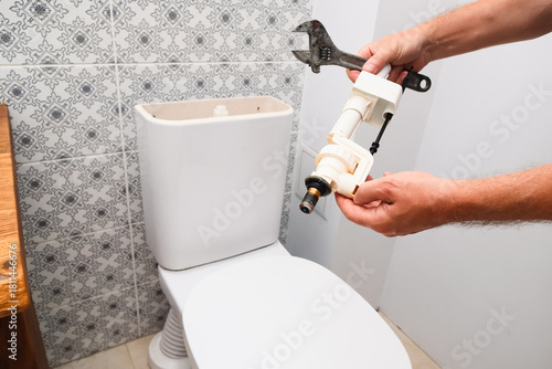 Plumber repairing toilet cistern. Hand holding a new fill valve and adjustable wrench.