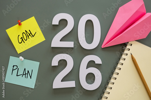 number of New Year 2026 with word goal and plan on post-it paper pin on green background, notebook, and paper plane symbolize New Year targets, resolutions, strategy, progress, and fresh starts.