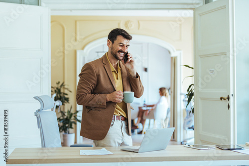 Smiling Businessman On Phone With Coffee In Modern Office At Desk