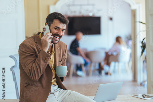 Smiling Man On Phone In Cozy Café With Laptop And Coffee Cup