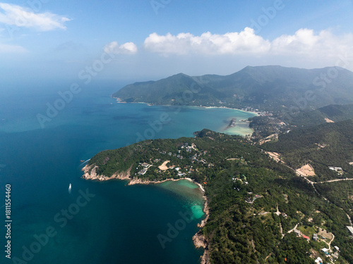Hilly coastline with turquoise bays and lush green forest under a bright sky. Ko Pha Ngan, Thailand.