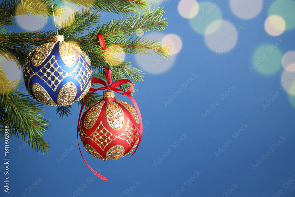 Obraz premium Christmas balls with pattern hanging on fir tree branches against blue background with blurred lights, closeup with space for text. Bokeh effect