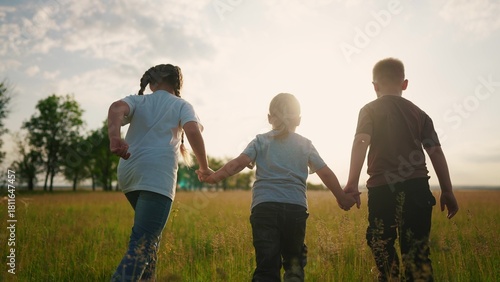 a group of children run across the field in the park. happy family childhood dream concept. several small children run across the grass and hold each lifestyle other's hands sunset shadows