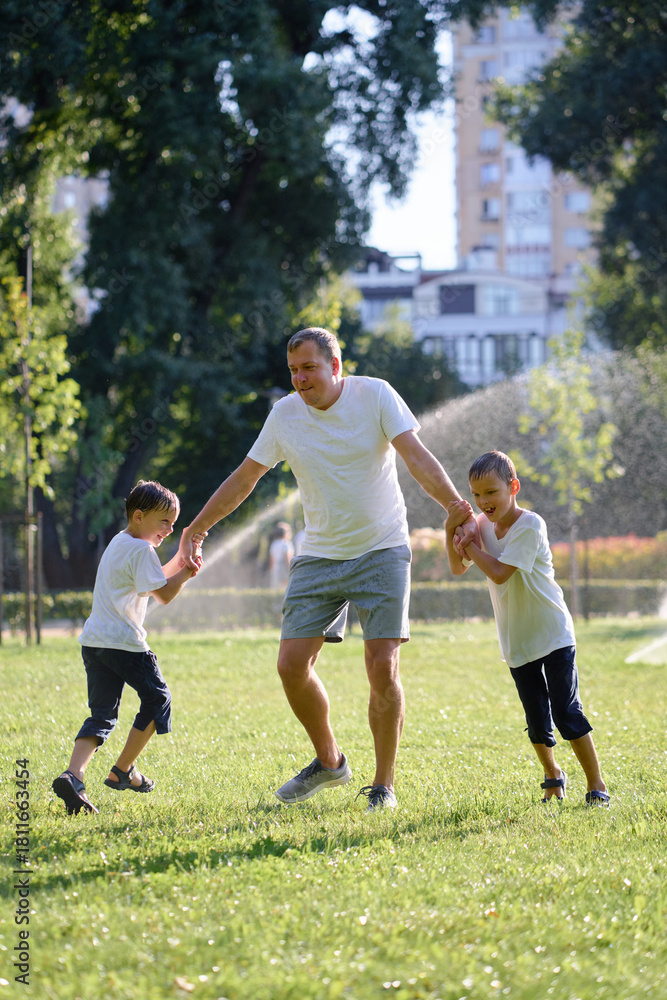 Obraz premium Father and his two young sons enjoying a playful moment together in a sunny green park. A display of joy and togetherness, perfect representation of family bonds during outdoor activities.