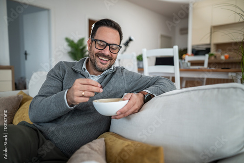 Man relaxing at home, smiling, eating snack on couch