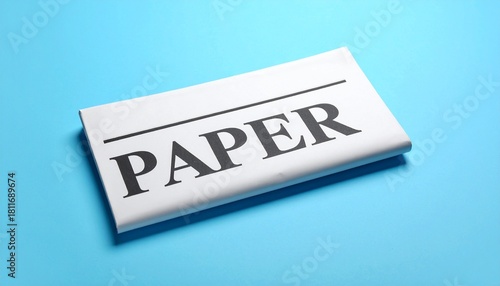 Folded newspaper with bold “PAPER” headline on blue surface.