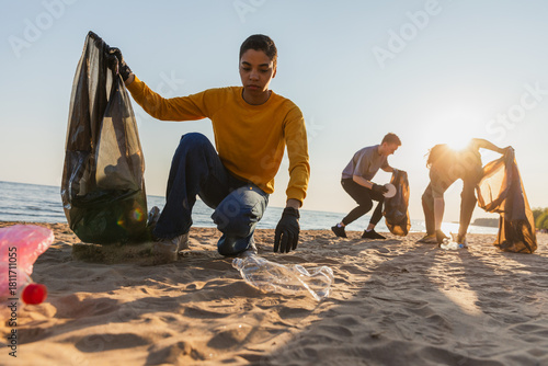 Earth day. Volunteers activists team collects garbage cleaning of beach coastal zone. Woman mans puts plastic trash in garbage bag on ocean shore. Environmental conservation coastal zone cleaning