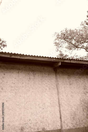 Cuadro en lienzo Sepia Toned Woven Bamboo Wall with Corrugated Metal Roofing Edge Building