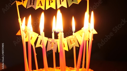 Happy birthday decoration on a cake with burning candles on dark background