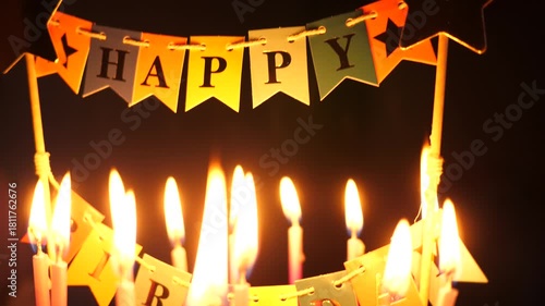 Happy birthday decoration on a cake with burning candles on dark background
