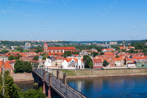 Cityscape panoramic view shows the old town of Kaunas, Lithuania. Red tiled rooftops and historic buildings line the Nemunas River and bridge in summer sunny day. Famous travel destination.