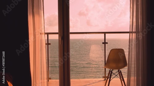 Beautiful Ocean View from the Balcony Patio Window of a Beachfront Room at Colorful Pink Orange Sunset Sky Clouds Sun, Chair, Curtain, Resort Hotel Room, Beach House in Sunlight.