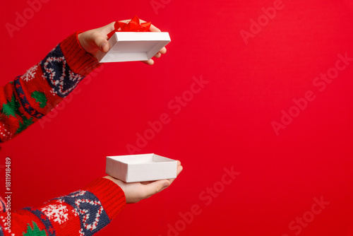 Hands opening a white gift box with red bow on a clean red background, perfect for holiday visuals, copyspace layouts, and seasonal campaigns