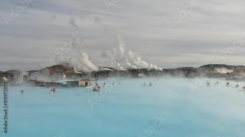 People enjoy soaking in warm, mineral-rich waters at a geothermal spa in Iceland. The sun sets, casting a beautiful glow over the steam rising from the water.