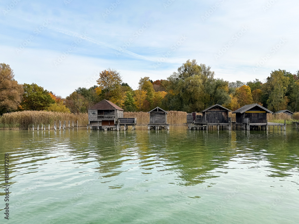 Obraz premium Wooden boathouses on stilts over calm lake water in autumn nature landscape