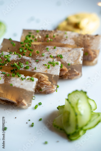 Fényképezés Close-up of aspic slices garnished with chopped herbs on a white plate with cucumber garnish