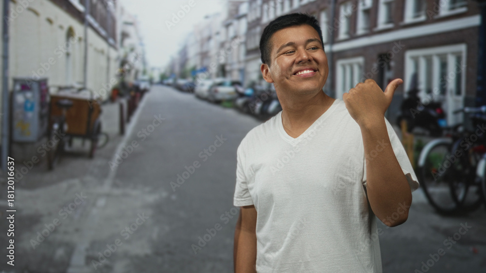 Fototapeta premium Hispanic young man pointing thumb over shoulder on street while smiling; casual confidence happiness.