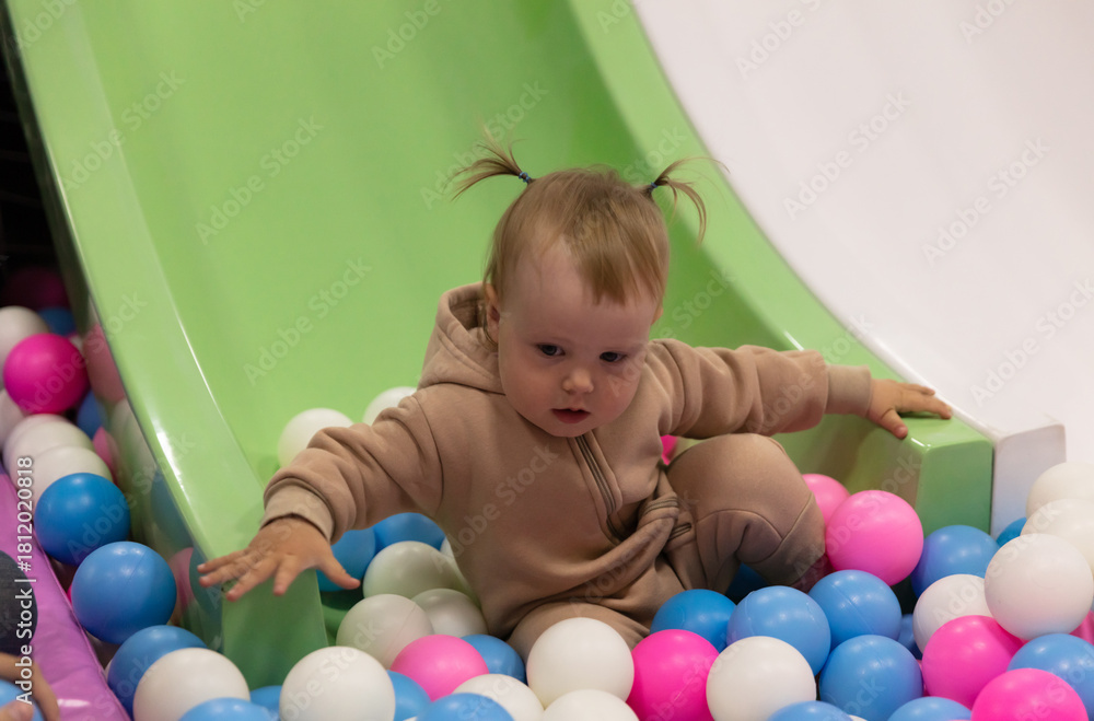 Obraz premium Little baby slides down a slide into a dry pool with balls at a children's entertainment center