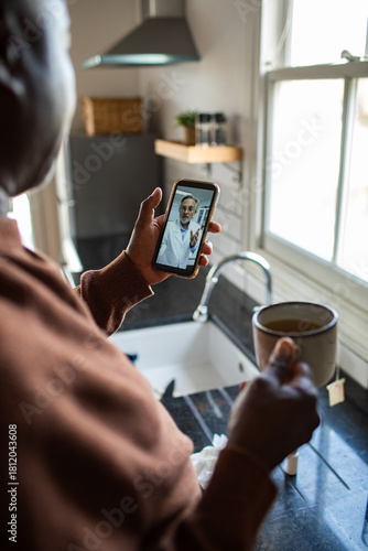 Adult focused on telehealth call with mature doctor in kitchen